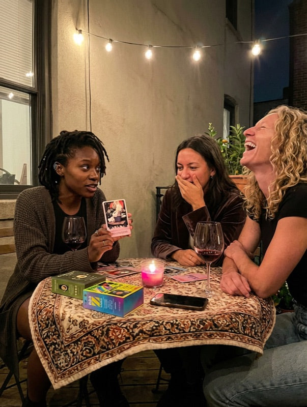 Three friends laughing on a rooftop with a Millennial Tarot card